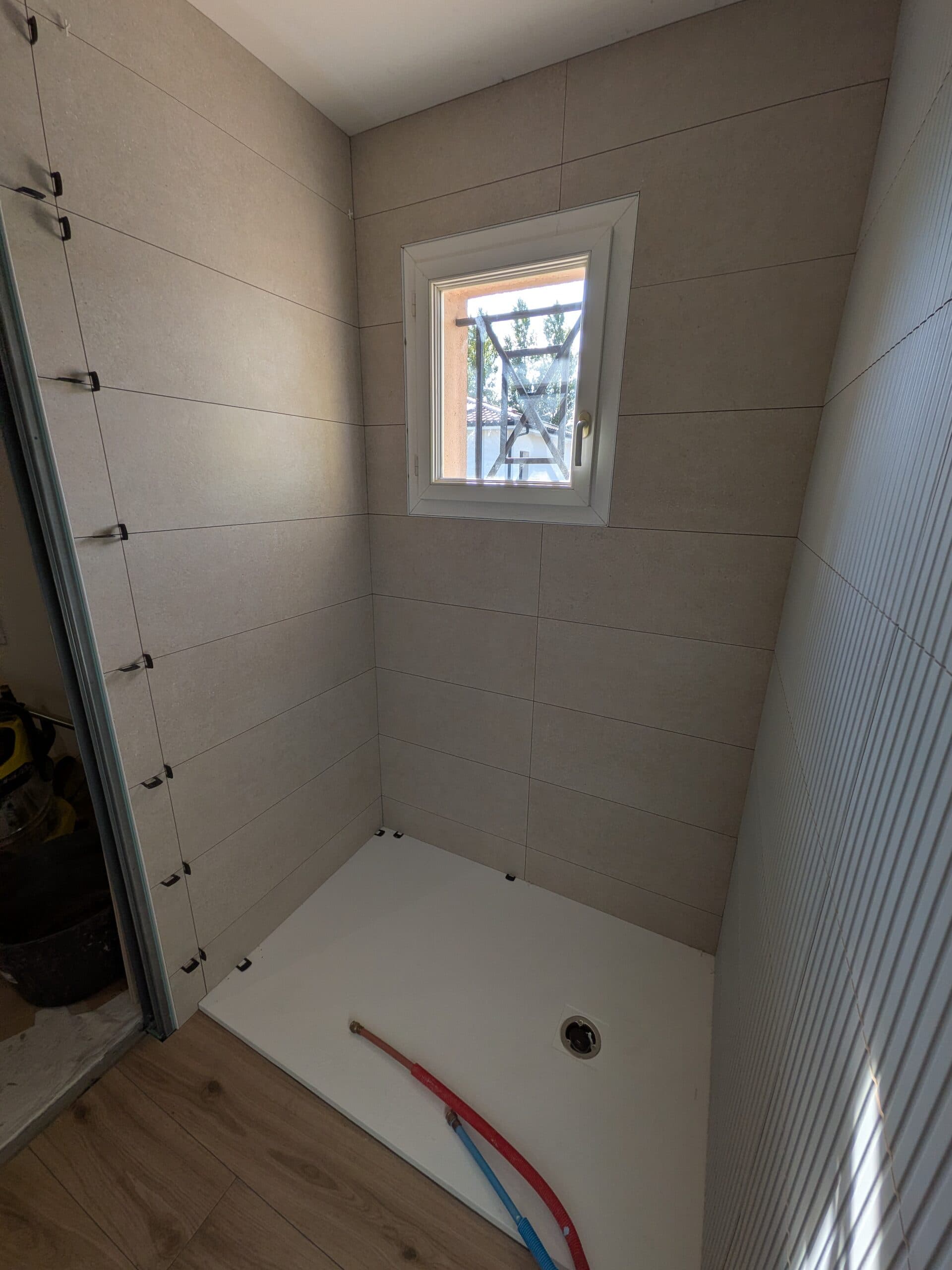 Pose de la faïence beige 30x90 autour de la fenêtre au-dessus du receveur, croisillons de calage encore en place
