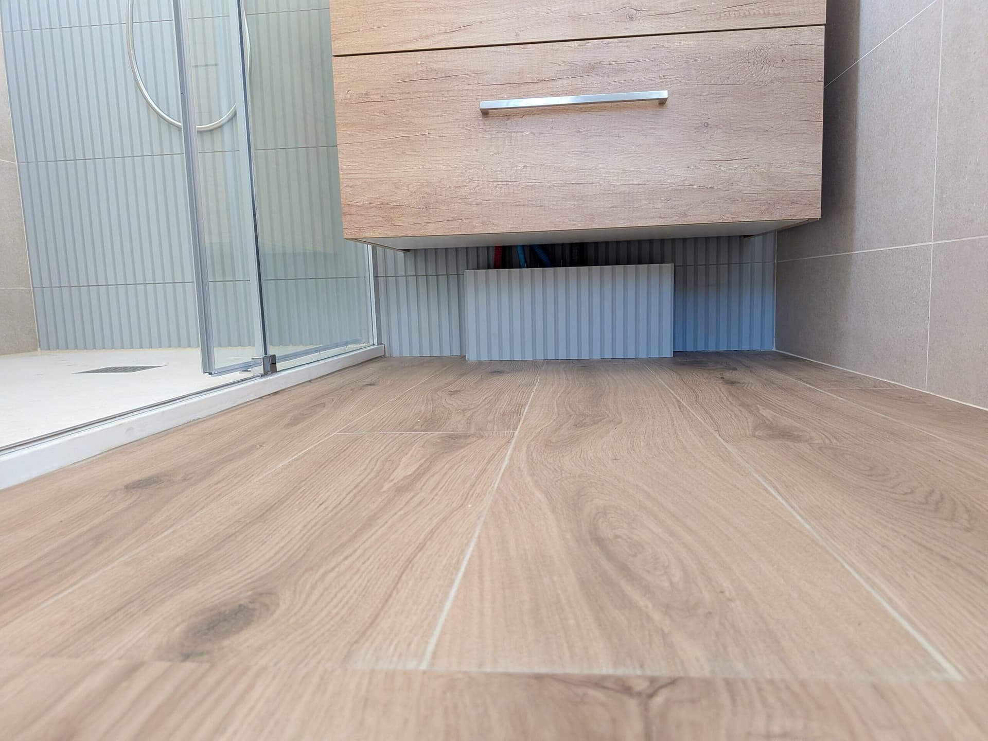 Carrelage imitation parquet 20x120 au pied du meuble vasque suspendu et de la paroi de douche coulissante