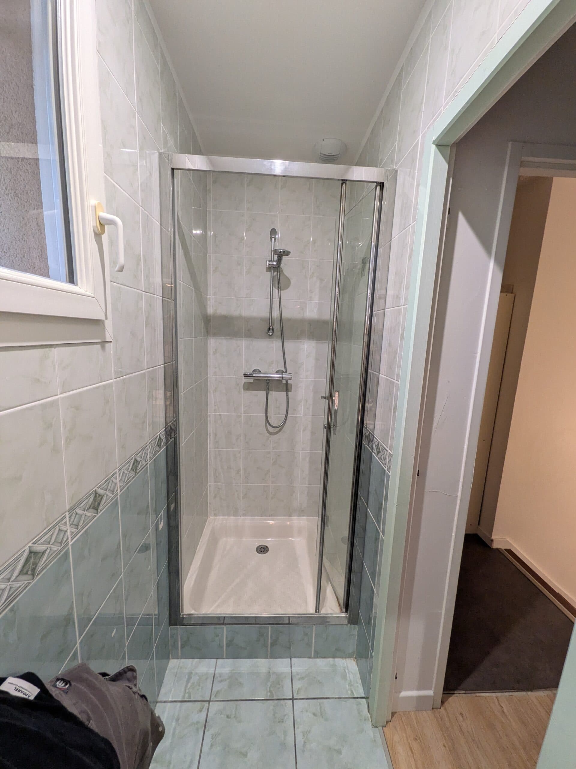 Première salle de bain avant travaux, ancienne cabine de douche au fond de la pièce étroite, faïence et frise d'origine