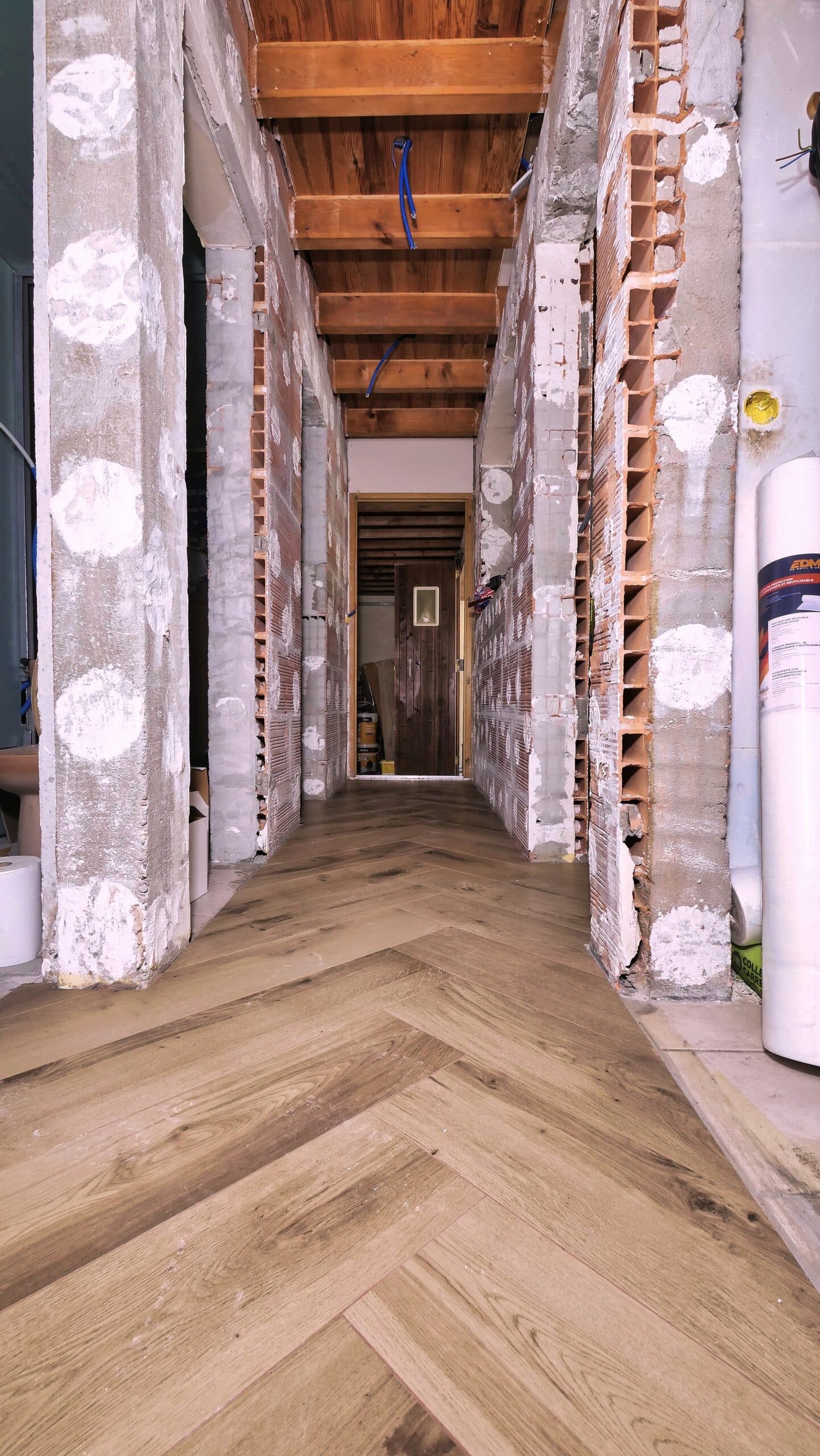Chevrons du carrelage effet chêne filant jusqu'au bout du couloir, raccord avec l'ancien carrelage en limite de chantier
