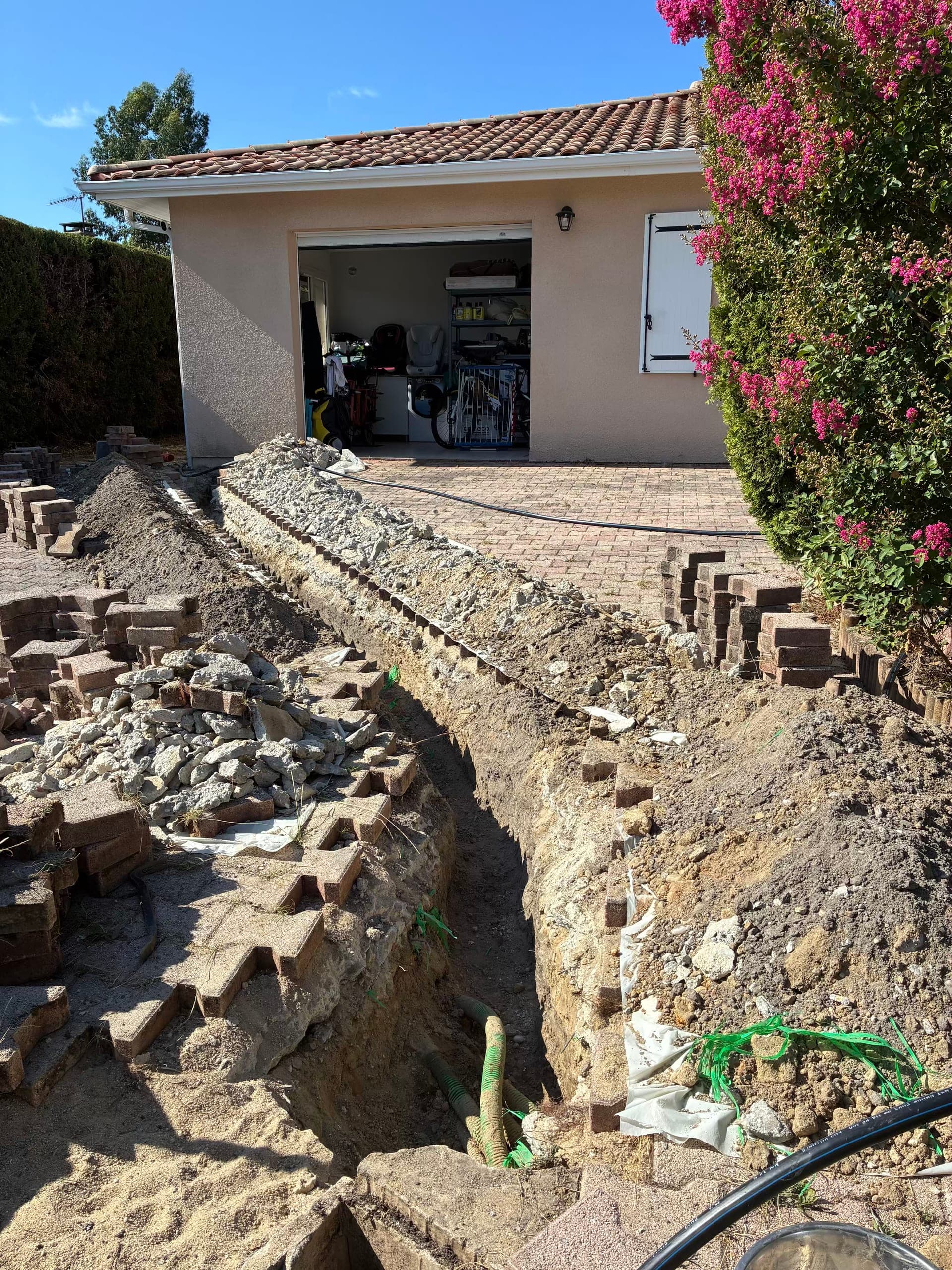 Tranchée ouverte dans l'allée pavée entre le compteur d'eau et le pied de maison, pavés déposés et rangés sur le côté