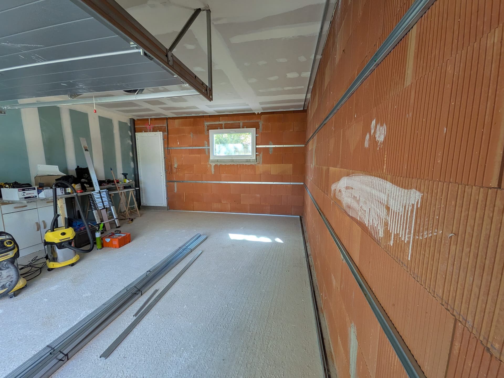 Ossature Optima en cours de pose sur le mur des menuiseries et sur le grand mur, profilés métalliques au sol