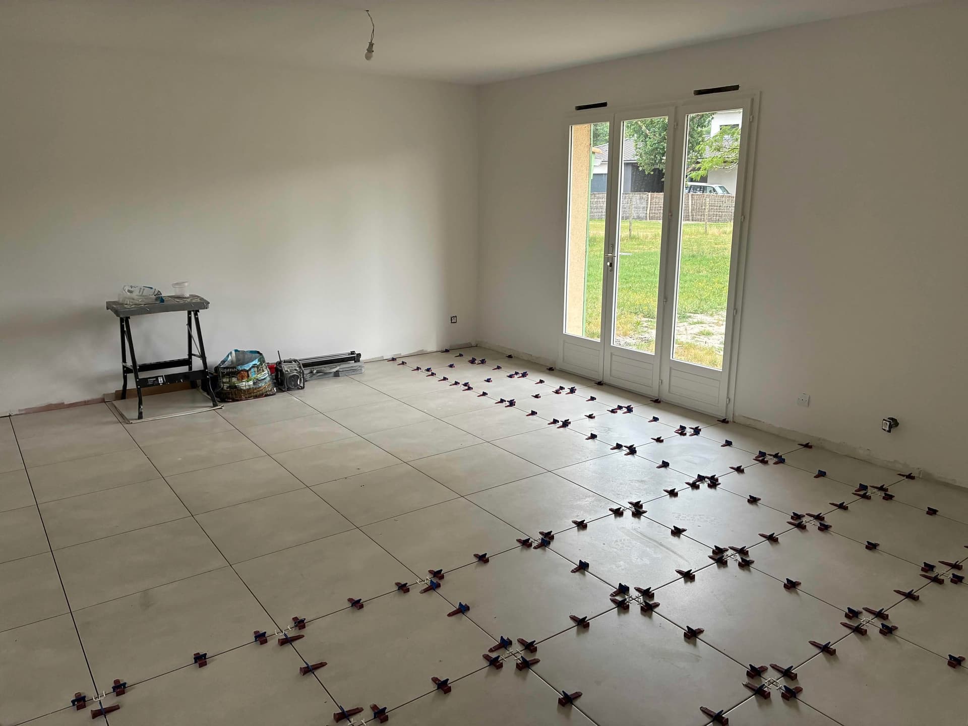 Pièce à vivre en cours de carrelage, croisillons autonivelants encore en place sur les carreaux 60x60